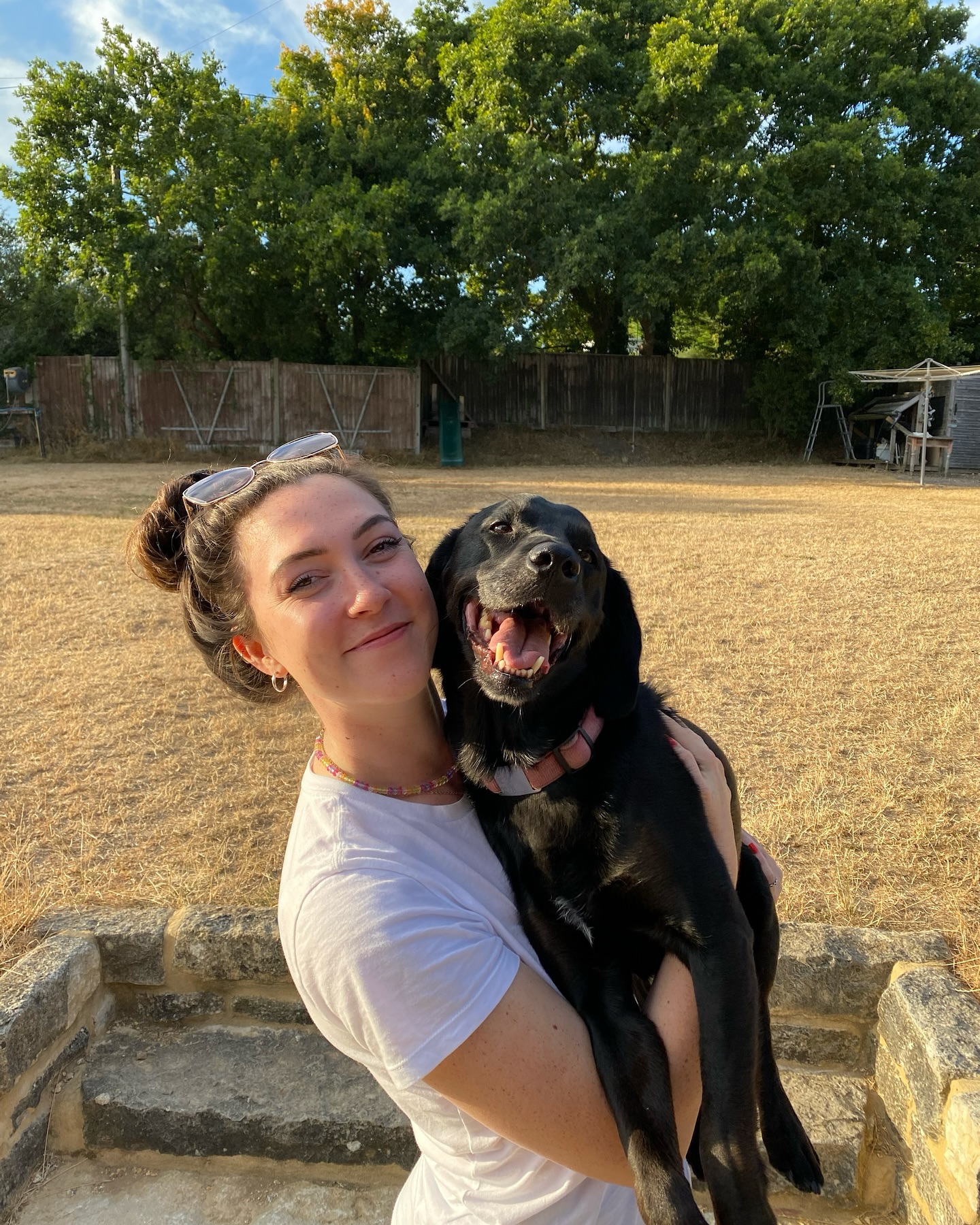 Alice, owner of Loolaah's Dog Grooming, smiling with a black Labrador in a sunny garden